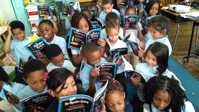 A group of students gather for floor time, examining their own copies of "The Digestive System."